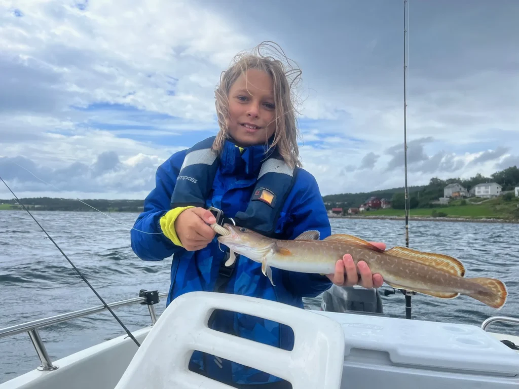 Kind mit Rettungsweste hält einen gefangenen Fisch im Angelboot auf dem Romsdalfjord