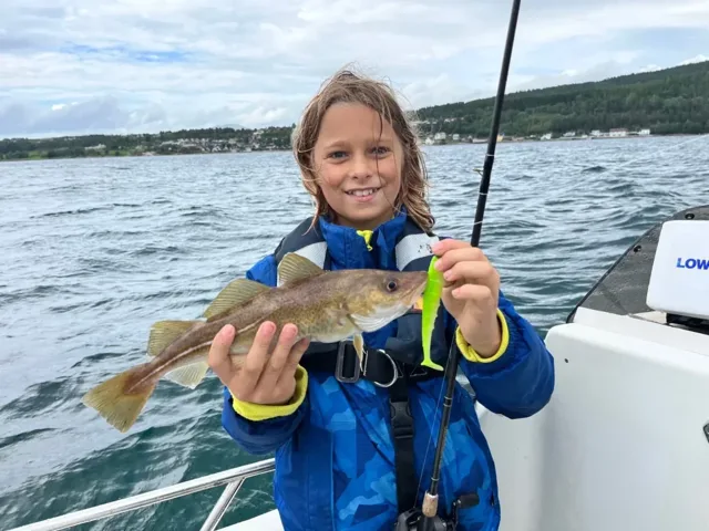 Kind mit Rettungsweste zeigt einen gefangenen Fisch